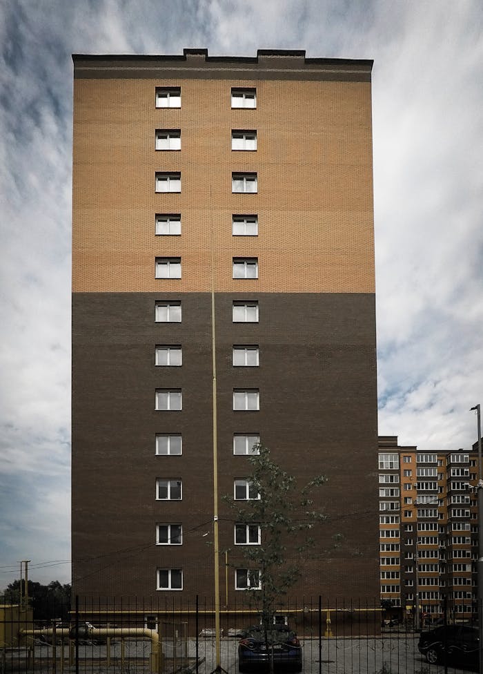 From below of exterior of modern multistory complex of houses located on city street under sky with clouds